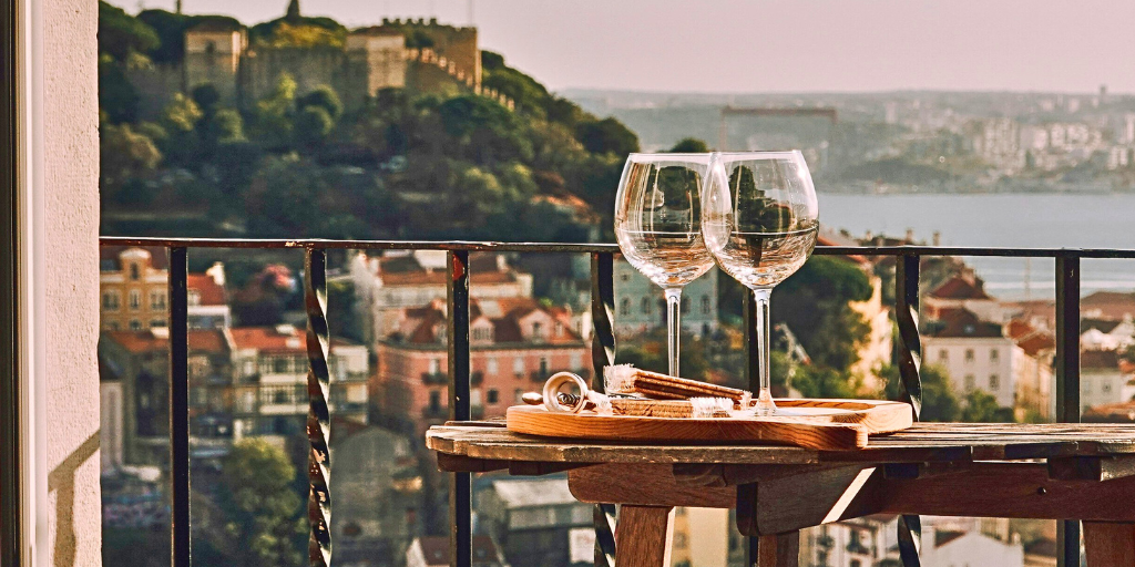 Two wine glasses on a hotel balcony overlooking a sunny landscape